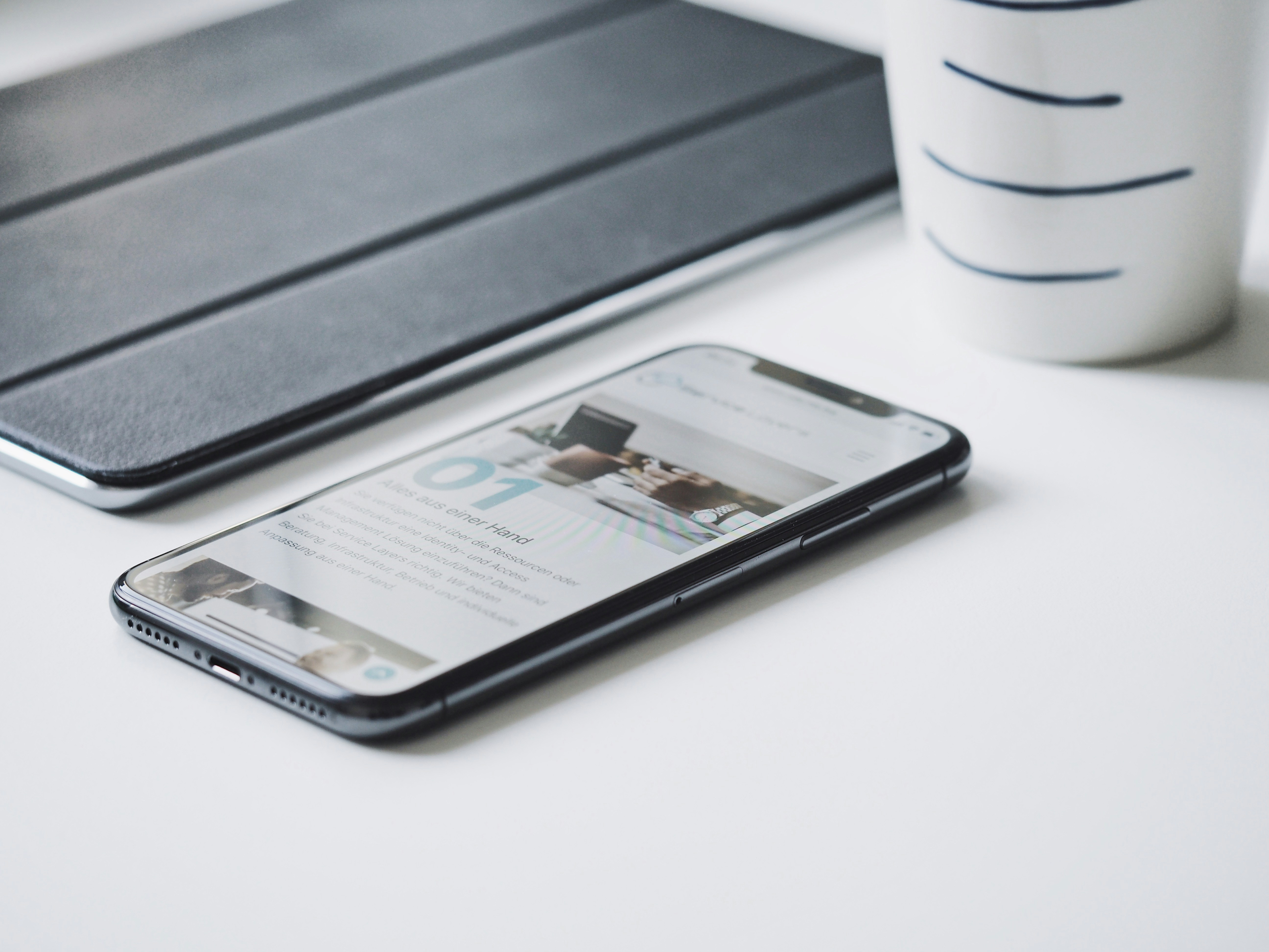iPhone with app content on desk next to iPad cover and white mug